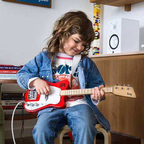 Front view of a child playing the mini red guitar.