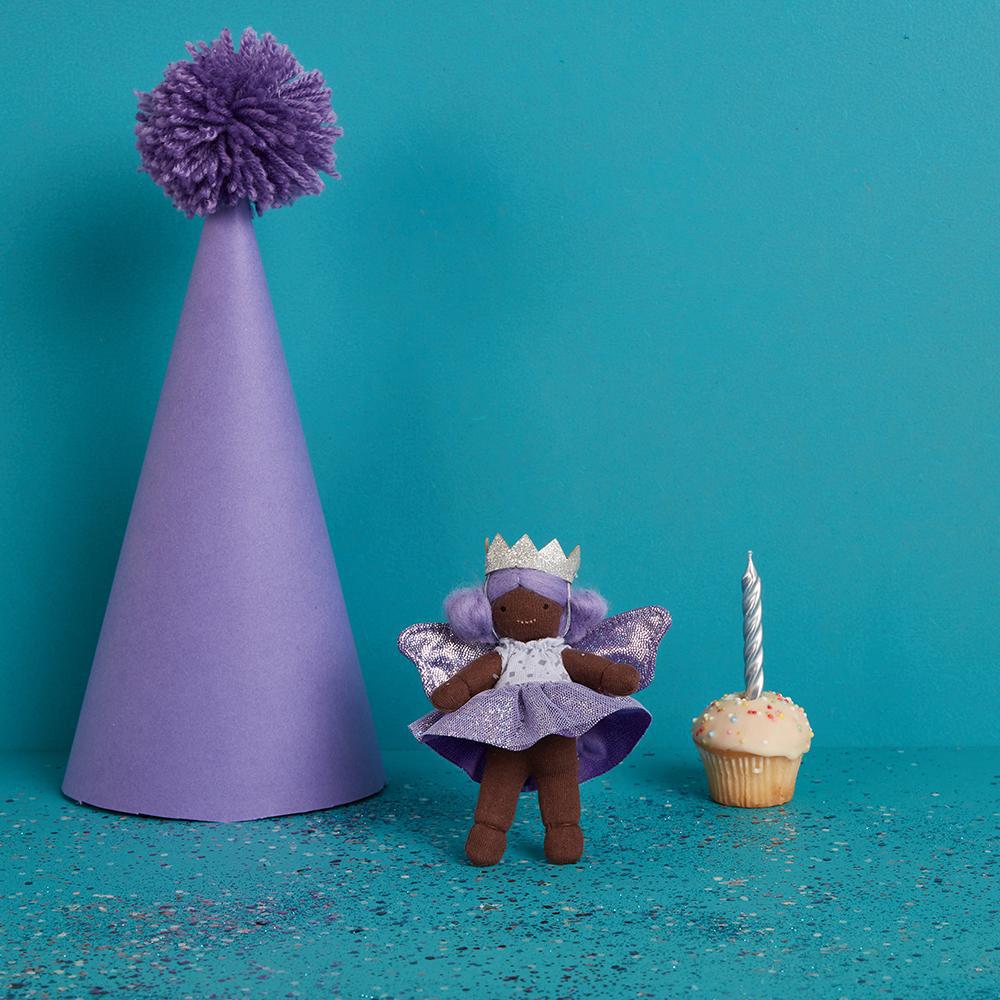 Front view of Bluebell The Birthday Fairy standing next to a life size purple party hat with a cupcake with a birthday candle in it.