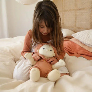 Front view of a young girl in the bed holding the Birdie Doll.