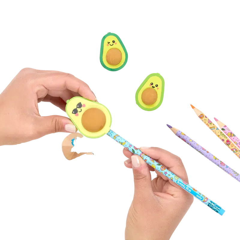 Front view of avocado sharpener being held in a person&#39;s hand with a pencil in it being sharpened while the avocado erasers lay beside with 3 pencils.