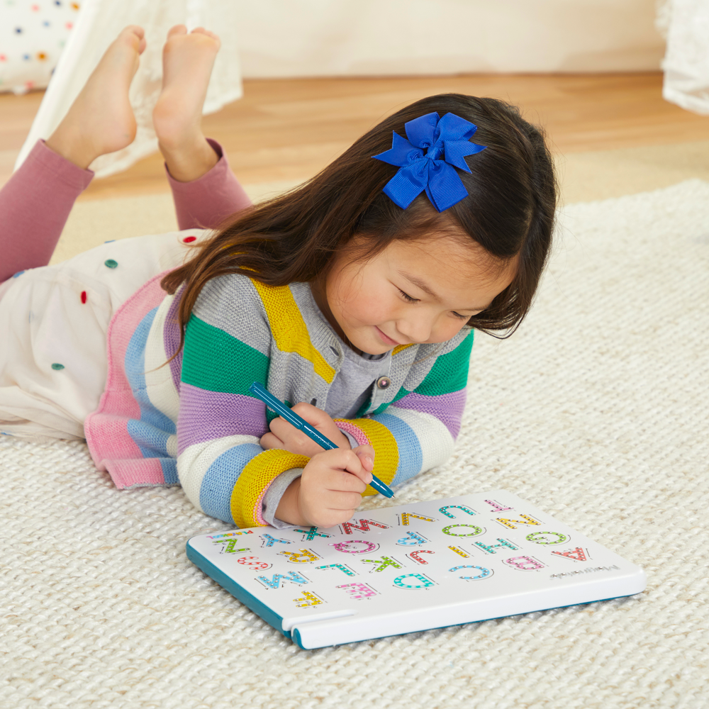 Front view of a little girl laying on her belly playing with the Magnatab A to Z Uppercase board.