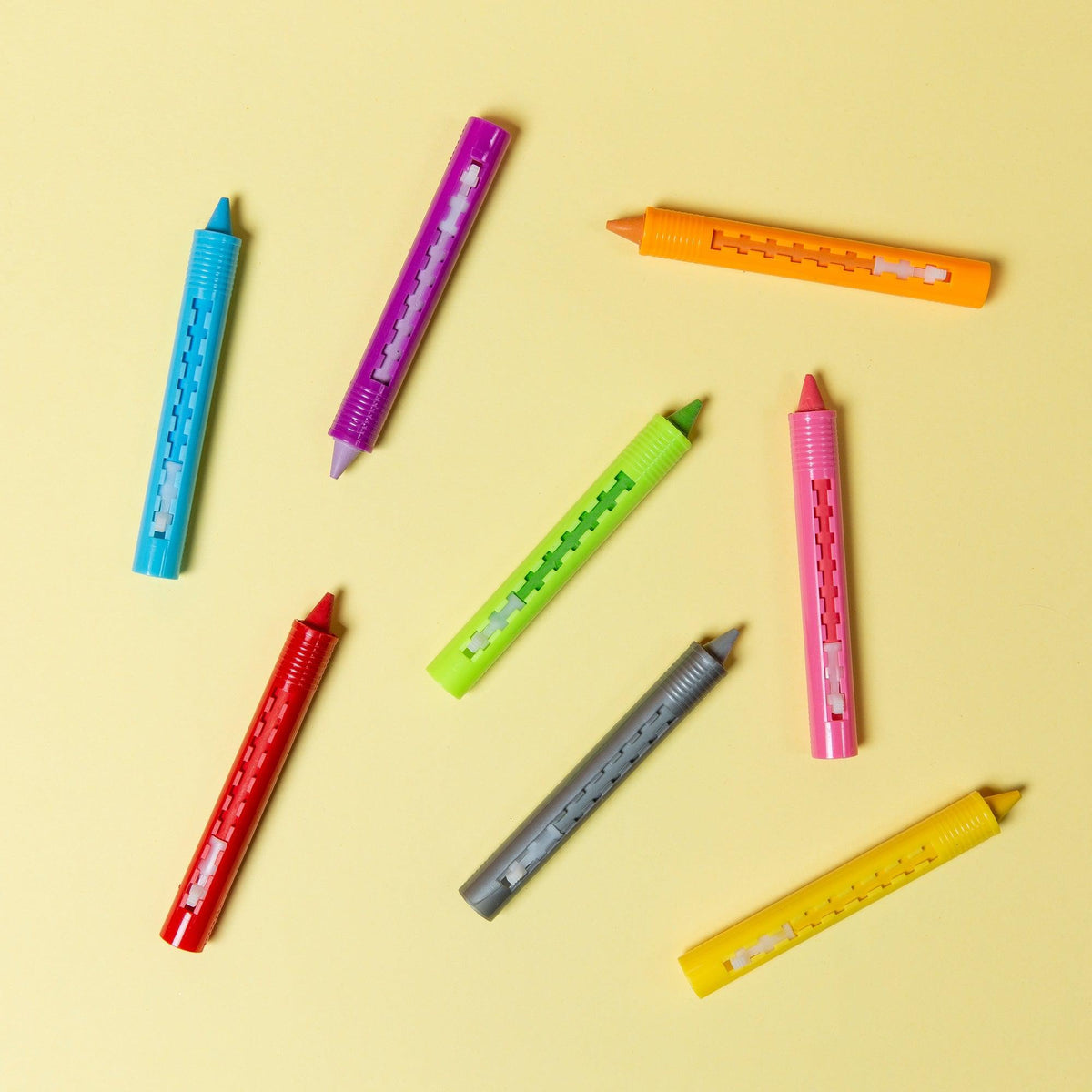 Front view of scattered bath crayons on yellow background showing colors blue, purple, orange, pink, green, red, silver, and yellow.