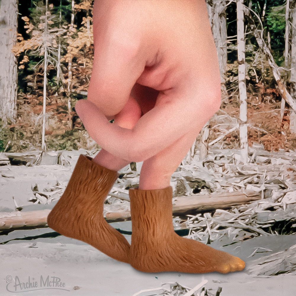 Front right side view of a hand with 2 fingers inside of a left and right Bigfoot finger puppet walking through a forest.