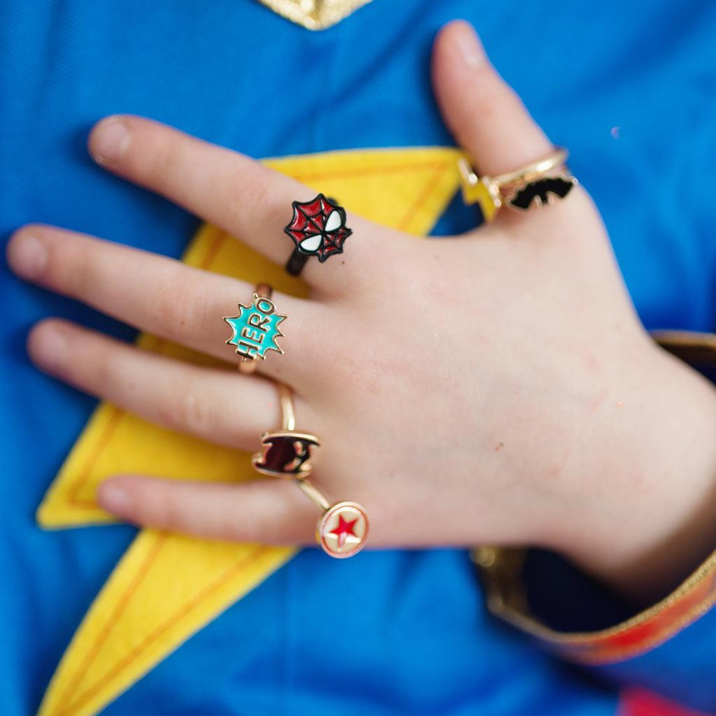 five adjustable metallic rings, each with a different inlayed super-hero symbol - yellow lightning bolt, black bat, red shield, black Batman helmet, red Spiderman mask. 