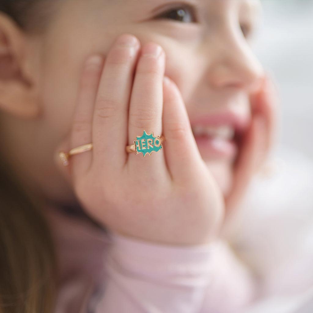 Smiling child, chin in hands, and HERO ring on ring finger 