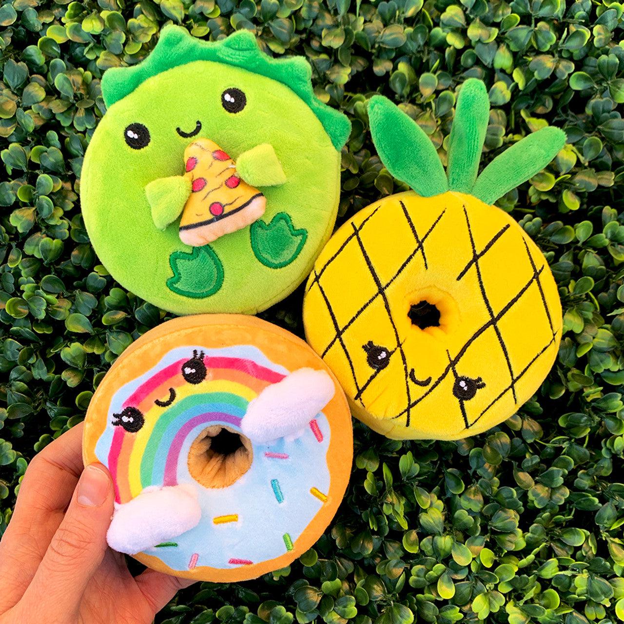 All 8 circular donut shaped plushies. Rainbow unicorn, green dinosaur with pizza, pastel cat with sunglasses and ice cream, shark, rainbow with clouds and sprinkles, pineapple, pastel narwal, pink cat with blue fish tail