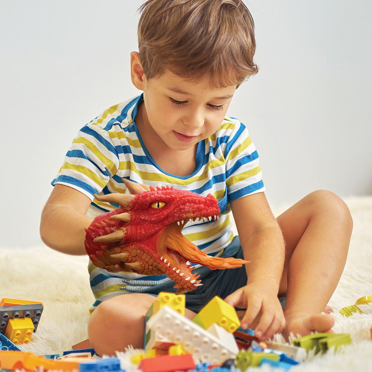 Front view of a child playing with a red dragon hand puppet.