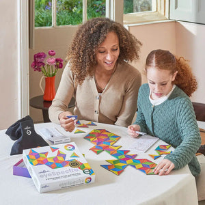 Front view of a woman and child sitting at a table playing eyeSpectro with the box and contents showing.
