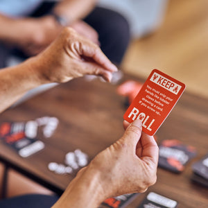 Front view of a person holding a lobster mobster card in one hand and acting out the prompt on the card with the other hand.
