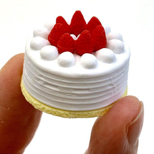 Front view of the white round cake with strawberries on top being held in someone's fingers from the Puzzle Eraser-Dessert.