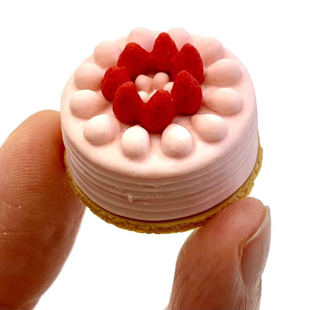 Front view of the pink round cake with strawberries on top being held in someone&#39;s fingers from the Puzzle Eraser-Dessert.
