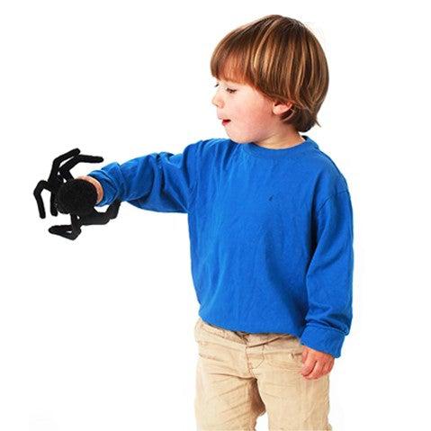 Black fuzzy spider finger puppet held by a child in a bright blue shirt.