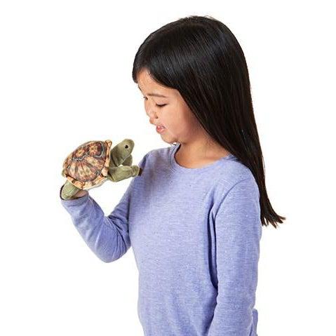 tortoise finger puppet held by a girl in a purple shirt.